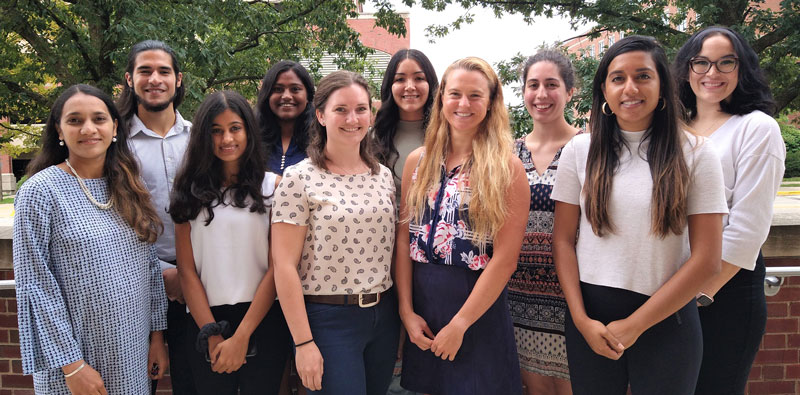 9 graduate students standing outside back entrance of Huff Hall with Professor Neha Gothe